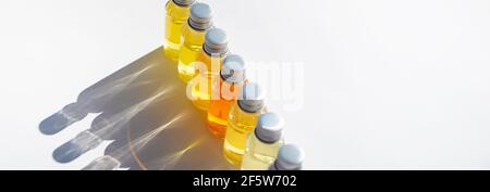 Fläschchen mit farbiger Flüssigkeit sind in einer Reihe angeordnet. Lockige Schatten fallen auf einen weißen Hintergrund. Stockfoto