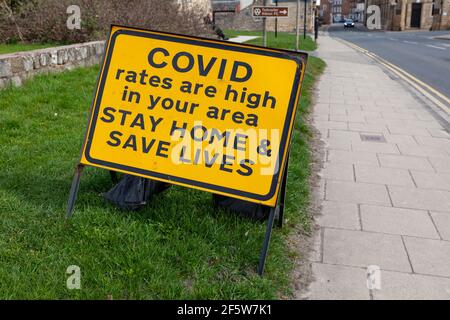 Covid 19 gelb und schwarz Warnschild am Straßenrand - hohe Preise, zu Hause bleiben, Leben retten Stockfoto