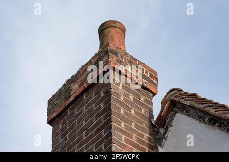 Detailansicht eines stark verwitterten und rissenden Ziegelsteinschornsteins und Kaminkänfels. Der Topf zeigt Anzeichen von Rissbildung und das Mauerwerk ist verwittert. Stockfoto