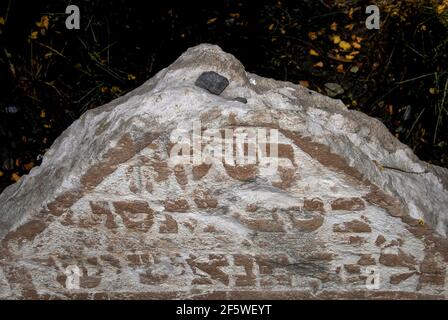 Auf diesem alten Grabstein wurden nach jüdischer Tradition und Tradition Steine hinterlassen, die darauf hindeuten, dass jemand das Grab auf dem Alten Jüdischen Friedhof in Josefov, dem Jüdischen Viertel in Prag, der Hauptstadt Tschechiens, besucht hat. Der Grabstein, mit einer hebräischen Inschrift in Relief geschnitzt, ist unter etwa 12.000 über fast 350 Jahre in den ummauerten Stadtkern gepfercht, mit rund 100.000 Einwohnern des ehemaligen Ghettos, die in bis zu 12 Schichten darunter liegen. Der früheste Grabstein stammt aus dem Jahr 1439 und die letzte Einlage war im Jahr 1787. Stockfoto