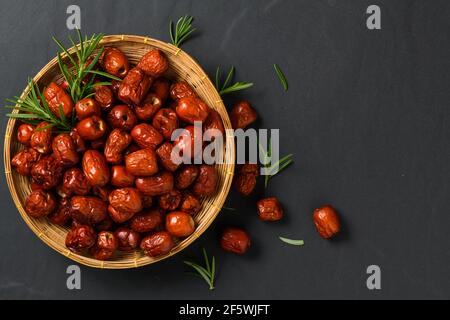 Getrocknete Jujube, chinesische getrocknete rote Dattobst mit Rosmarinblatt in Bambuskorb auf schwarzem Hintergrund, Kräuterfrüchte. Es hat mehr Vitamin C, das f hilft Stockfoto