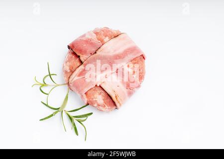 Hamburger mit Speck auf einem weißen Teller mit einem Zweig Rosmarin. Roher Hähnchen-Hamburger. Stockfoto