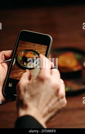 Ein Mann mit einem Telefon in der Hand macht ein Foto Von einem Kuchen in einem Restaurant Stockfoto