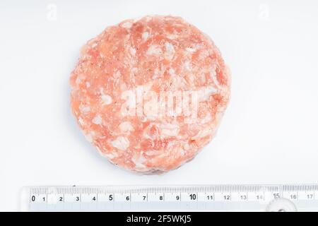 Chicken Hamburger Nahaufnahme mit einem Lineal für die genaue Größe des Kalibers auf weißem Hintergrund. Roher Hähnchen-Hamburger mit Platz für Text. Stockfoto