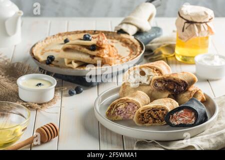 Mehrere Pfannkuchen mit verschiedenen Füllungen auf einem Teller auf einem hölzernen weißen Hintergrund Seitenansicht mit einem Kopierplatz für den Text. Traditionelles Essen für die Ma Stockfoto