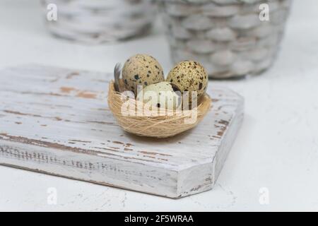 Drei Wachteleier in einem Nest auf einem weißen Schneidebrett auf Beton. Osterkonzept. Stockfoto