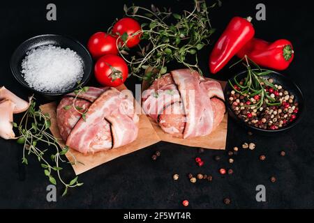 Zwei Hähnchen-Hamburger, eingewickelt in Speck auf Höhlenpapier mit Rosmarinzweigen, schwarzem Pfeffer, süßen roten Paprika, Tomaten und Knoblauch auf einem schwarzen Backgrou Stockfoto