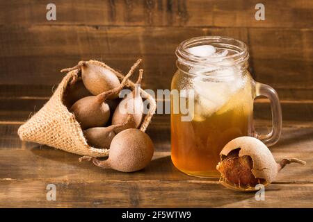 Tamarindensaft in einem Glas, umgeben von frischen reifen Tamarinden - Tamarindus indica Stockfoto