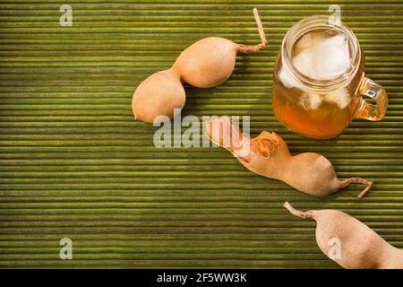 Tamarindensaft in einem Glas, umgeben von frischen reifen Tamarinden - Tamarindus indica Stockfoto