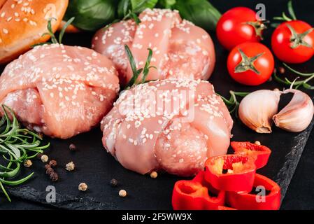 Nahaufnahme von drei Hähnchen-Hamburgern mit Rosmarinzweig, roten Paprika, Kirschtomaten und einem Hamburger-Brötchen auf schwarzem Hintergrund. Fast Food. Komfort Stockfoto