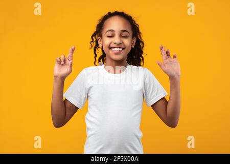 Hoffnungsvolles afroamerikanisches Mädchen, das ihre Finger kreuzt Stockfoto