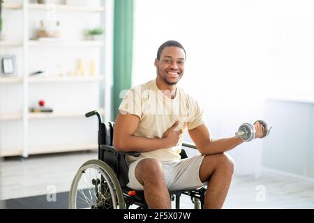 Körperliche Rehabilitation für behinderte Menschen. Behinderter schwarzer Kerl im Rollstuhl, der zu Hause mit Hantel Exerises macht Stockfoto