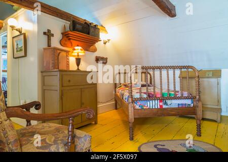 Einzelbett mit buntem Patchwork-Bettüberwurf, antike Kommode aus Holz, tiffany-Lampe, gepolsterter Sessel mit blumigen Motiven im Schlafzimmer Stockfoto