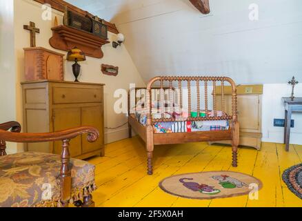 Einzelbett mit buntem Patchwork-Bettüberwurf, antike Kommode aus Holz, tiffany-Lampe, gepolsterter Sessel mit blumigen Motiven im Schlafzimmer Stockfoto