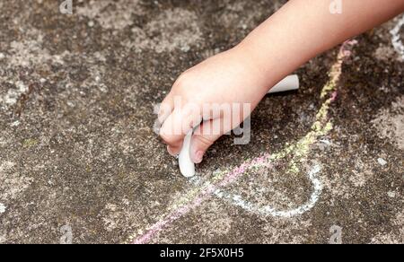 Kleine Kinderhand, Mädchen mit weißer Kreide, Zeichnung, Schreiben auf den Beton draußen. Schulalter Kind Zeichnung mit Kreide auf dem Boden im Freien, han Stockfoto