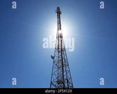 Blick aus dem niedrigen Winkel auf den Mobilfunkturm oder den Mobilfunkturm gegen die Sonne am blauen Himmel. Stockfoto
