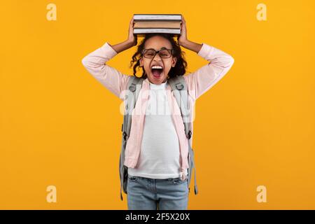 Schreiendes schwarzes Mädchen, das Stapel Bücher auf ihrem Kopf hält Stockfoto