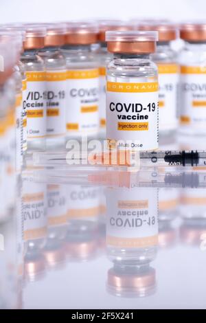 Coronavirus-Impfstofffläschchen und eine Spritze auf einem weißen Tisch mit Reflexionen und anderen Fläschchen im Hintergrund. Labor- oder Gesundheitseinrichtungen Stockfoto
