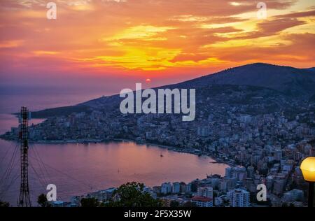 Saranda/Albanien – 1. August 2020: Luftpanorama Stadtbild auf Sonnenuntergang, Meer, Berge, bunten Himmel, Outdoor-Café und Menschen, genießen die Aussicht Stockfoto