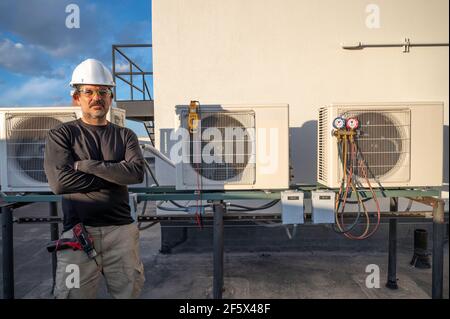HLK-Techniker steht neben Klimaanlagen, negativer Raum an der Wand Stockfoto