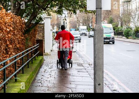 CHELSEA, LONDON, ENGLAND - 17th. Februar 2021: Royal Mail Postarbeiter schiebt einen Postwagen in Chelsea Stockfoto