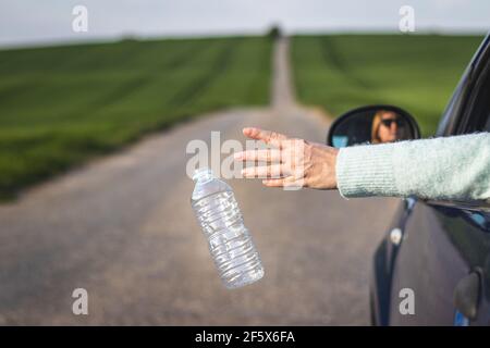 Der Fahrer warf die Plastikflasche vom Autofenster auf der Straße weg. Umweltschutz. Konzept der Kunststoffverschmutzung Stockfoto