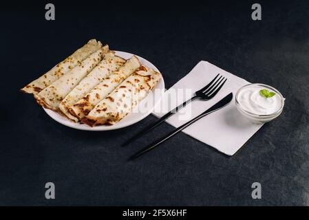Pfannkuchen auf schwarzem Teller mit Besteck. Pfannkuchendessert. Stockfoto