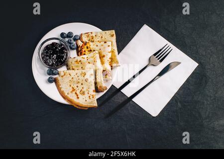 Pfannkuchen auf schwarzem Teller mit Besteck. Pfannkuchendessert. Stockfoto