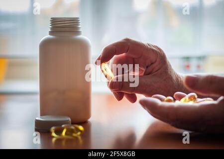 Ältere Frau hält Omega-3 Nahrungsergänzungsmittel Kapsel in der Hand. Flasche mit medizinischen Pillen im Hintergrund. Einnahme von Medikamenten Stockfoto