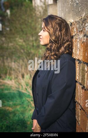 Portrait von schönen braunen Haaren junge Frau lehnte Wand. Stilvolle kaukasische Frau trägt schwarze Jacke Stockfoto