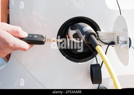 Laden eines Elektrofahrzeugs mit eingestecktem Netzkabel In und mans Hand entsperren es mit einem Schlüssel Stockfoto