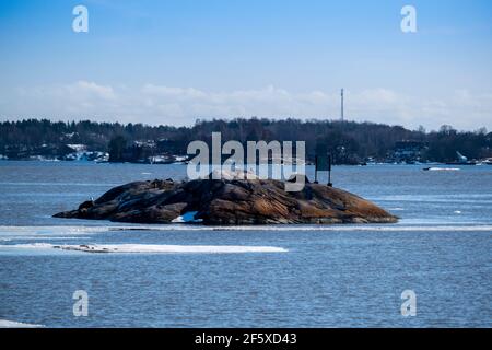 Ein kleiner Skerry in der Mitte eines Flusses mit einer großen Insel im Hintergrund. Stockfoto
