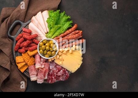 Große Auswahl an Wurst und Käse auf einem runden Brett auf braunem Hintergrund. Stockfoto