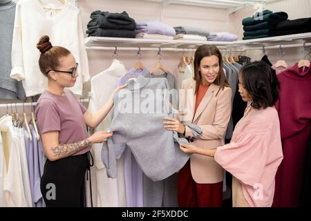 Zwei Verkäuferinnen schlagen dem Kunden beim Einkaufen einen neuen Jumper vor Im Bekleidungsgeschäft Stockfoto