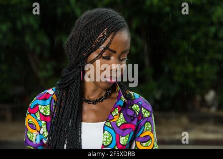 Junges afrikanisches Mädchen, das unter einem leichten Regen steht und etwas anstarrt. Stockfoto