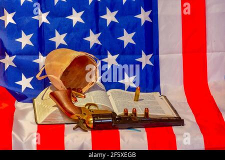 Die geöffnete Heilige Bibel, Bulle Hodensack, Kugeln und Revolver auf der amerikanischen Flagge Stockfoto