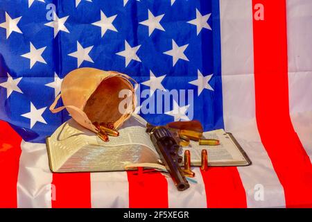 Die geöffnete Heilige Bibel, Bulle Hodensack, Kugeln und Revolver auf der amerikanischen Flagge Stockfoto