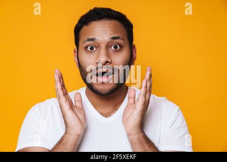 Asiatische Brünette unrasiert überrascht Mann Heben Hände zu seinem Gesicht Isoliert auf gelbem Hintergrund Stockfoto