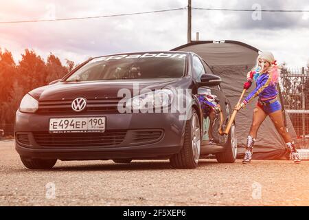 Moskau, Russland - 06. Juli 2020: Harley Quinn trifft mit einem Baseballschläger auf ein geparktes schwarzes Auto. Es ist eine Delle im Auto, das Auto ist beschädigt. Cosplay, Mädchen verkleidet als Charakter Kostüm Stockfoto