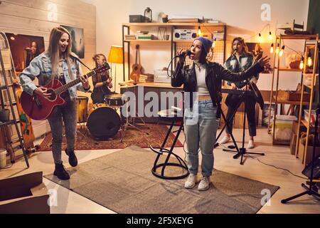 Junge Sängerin singt im Mikrofon mit anderen Musikern, die spielen Gitarre und Schlagzeug während der Aufführung Stockfoto