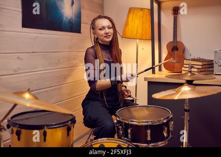 Porträt einer jungen Frau mit stilvollen Frisur lächelt an der Kamera Während des Lernens, Schlagzeug im Studio zu spielen Stockfoto
