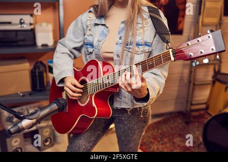 Nahaufnahme einer jungen Frau, die vor dem Mikrofon steht und Gitarre spielen im Aufnahmestudio Stockfoto