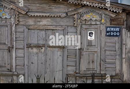 Alte verfallene Holzfassade des Hauses mit geschnitzten Verkleidungsbrettern, lockigen Wandelementen und Metallstangen, mit einem Schild Vorsicht Hund. Stockfoto