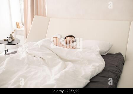 Junge schöne Brünette Frau friedlich schlafen in großen komfortablen Doppel Bett unter weißer Decke mit Kopf auf weichem Kissen Stockfoto