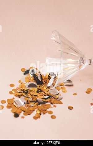 Weinglas mit Gold funkelt oder Konfetti auf rosa Hintergrund. Konzept der Feier. Stockfoto