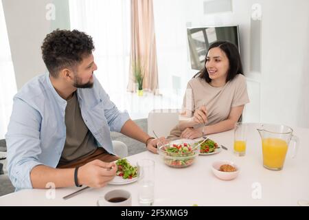Glücklich junge Brünette Frau Blick auf ihren Mann mit einem Lächeln Beide hatten selbst gemachten Gemüsesalat und Orangensaft Tabelle Stockfoto