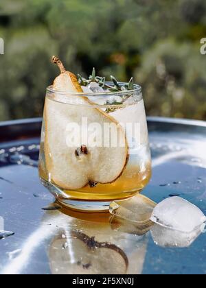 Frischer und gesunder Cocktail oder Mocktail mit Birne, Eis und Kräutern auf der Stahlschale. Erfrischendes Getränk im Garten. Stockfoto