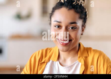 Ein Nahaufnahme-Porträt einer hübschen, schicken, afroamerikanischen Mixed-Race-jungen Frau mit Dreadlocks, Studentin oder Freiberuflerin, in lässiger Kleidung, mit freundlichem Lächeln auf die Kamera Stockfoto