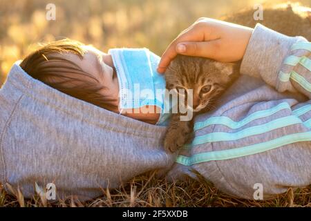 Kleines Mädchen mit Maske spielt mit ihrer Katze während der Coronavirus-Pandemie Stockfoto