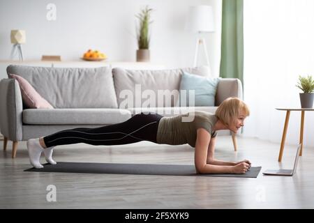 Seitenansicht der reifen Frau stehen in Ellenbogen Plank, Yoga Asana, Training zu Online-Sport-Video zu Hause, kopieren Raum Stockfoto